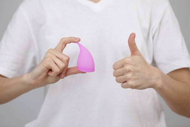 closeup hands of woman holding menstrual cup on white t-shirt background showing thumb up, having period, dislike to use napkins or tampons. selective focus - Фото, зображення
