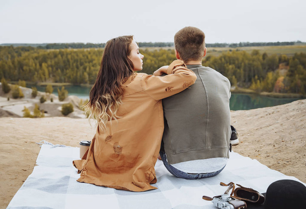 Happy couple sitting on a plaid and enjoying nature view. - Фото, изображение