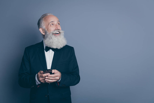 Portrait of his he nice attractive chic classy cheerful cheery glad gray-haired man wearing tux using device looking aside new idea isolated over dark grey pastel color background - Valokuva, kuva
