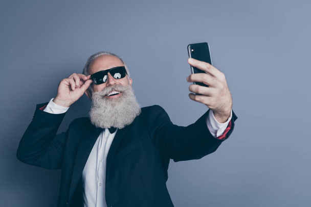 Close-up portrait of his he nice attractive chic classy cool trendy cheerful cheery gray-haired man touching specs taking making selfie influencer isolated over dark grey pastel color background - Foto, afbeelding