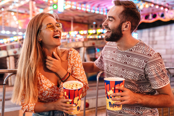 Loving couple walking in amusement park eat popcorn. - Фото, изображение