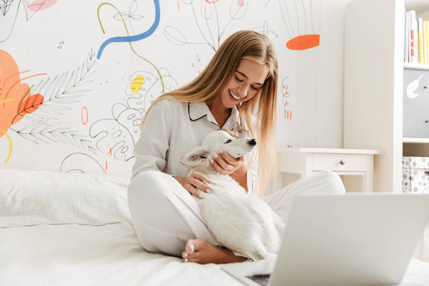 Cute girl in pajama at home on bed with her dog - Foto, Imagem