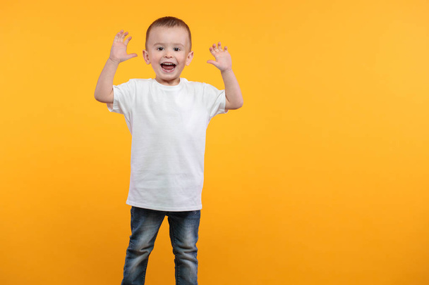 Παιδί αγόρι φορώντας λευκό t-shirt με χώρο για το λογότυπο ή το σχεδιασμό σας πάνω από κίτρινο φόντο - Φωτογραφία, εικόνα