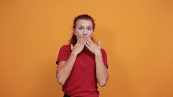 Zszokowana młoda dama w czerwonej koszuli przykrywającej usta dłońmi - Materiał filmowy, wideo
