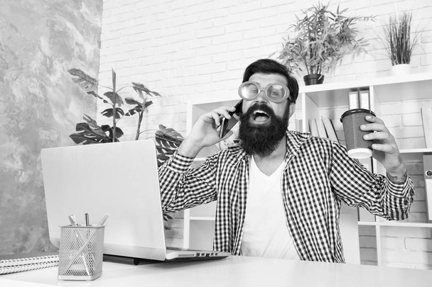 Cup of coffee is really about communication. Bearded man communicating by smartphone. Hipster working on computer with wireless communication in office. Using mobile communication. Communication - Photo, image