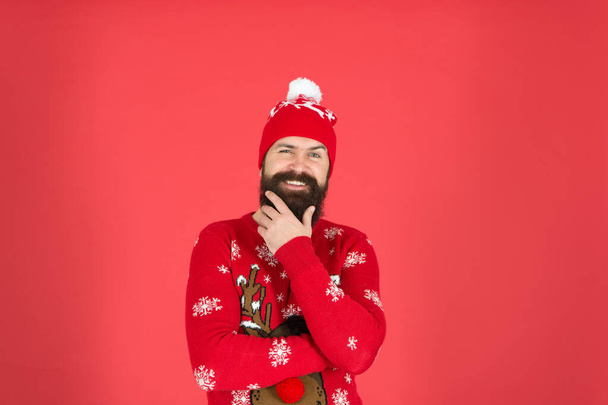 Bearded face close up red background. Cold days. Winter holidays. Man bearded hipster wear winter knitted hat. Barbershop and facial hair. Winter skin care. Guy wearing winter clothes and accessory - Photo, image