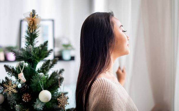 Happy asian woman standing near window in christmas decorated home - Zdjęcie, obraz