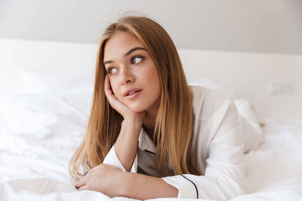 Photo of pretty blonde woman looking aside while lying on bed - Photo, image
