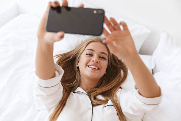 Photo of cheerful woman aking selfie photo on cellphone while lying - Fotoğraf, Görsel