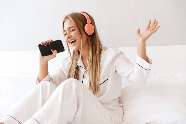 Photo of young happy woman listening music while singing - Foto, afbeelding