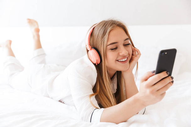 Photo of young pleased woman listening music while lying on bed - Foto, immagini