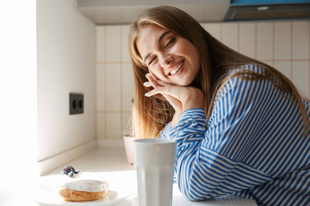 Image of attractive young girl smiling and drinking tea in kitch - Φωτογραφία, εικόνα