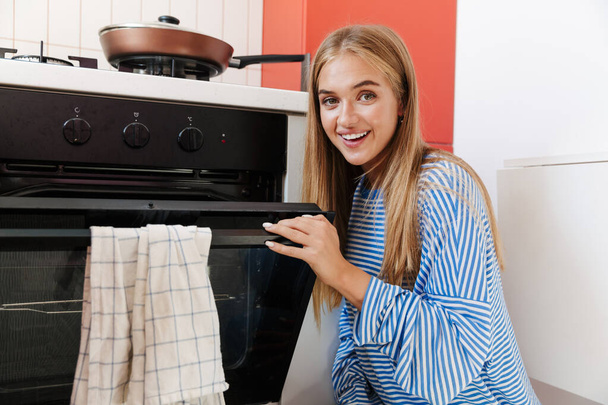 Image of pleased young girl using smiling while cooking in oven  - Valokuva, kuva