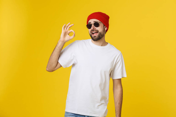Satisfied young man showing okay sign isolated on yellow background. - Фото, изображение