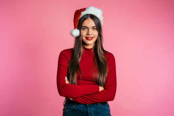 Attractive girl in Santa hat. Portrait of lady on pink background. Christmas or New year concept. Happy pretty woman smiling to camera. - 写真・画像