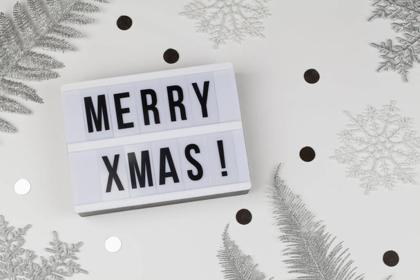 Frohe Weihnachten Worte auf Leuchtkasten mit weißen Schneeflocken, silberne Baumzweige auf weißem Hintergrund - Foto, Bild