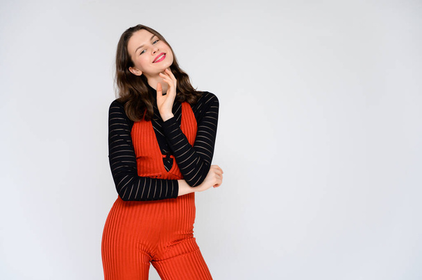 Concept adult girl on a white background. A photo of a pretty brunette girl in red trousers and a black sweater smiles and shows different emotions in different poses right in front of the camera. - Fotoğraf, Görsel