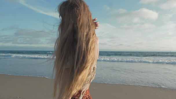 młoda kobieta z długimi włosami spacerująca po plaży - Materiał filmowy, wideo