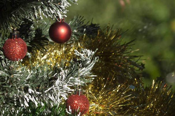 Μικρές κόκκινες μπάλες στο χριστουγεννιάτικο δέντρο που περιβάλλεται από λαμπερό κίτρινο tinsel - Φωτογραφία, εικόνα