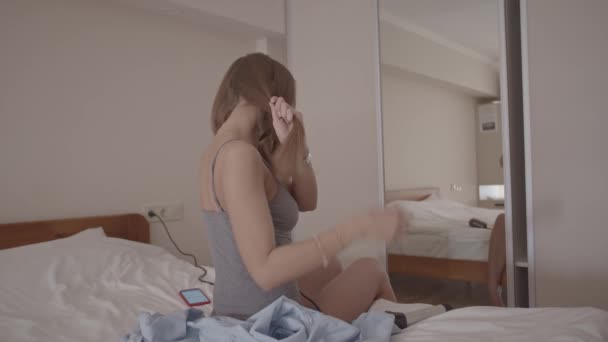 jonge vrouw op bed in slaapkamer styling haar haar kijken in spiegel, schot in slow motion - Video