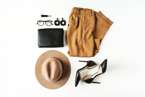 Women fashion clothes, accessories on white background. Flat lay, top view minimal trendy lifestyle collage. Pants, high-heel shoes, glasses, hat, purse bag, earrings. Fashion blogger concept. - Photo, Image