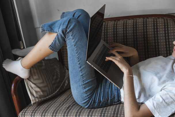 Woman with a laptop laying on a sofa. Study and work online, freelance. Self employed woman, girl working with her notebook laying on a couch with a phone, smartphone and ereader on table. - 写真・画像