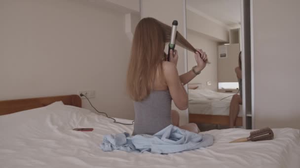 Young woman on bed in bedroom styling her hair looking in mirror, shot in slow motion - Video