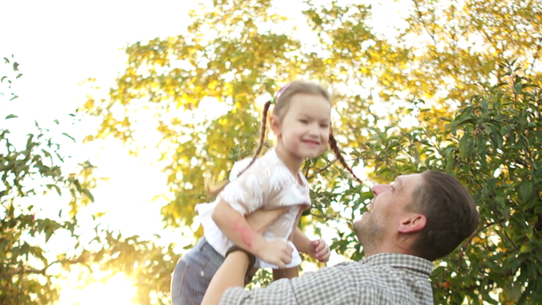 Der junge Mann wirft ein fünfjähriges Mädchen zur Welt. das Kind lacht und ist glücklich. glückliche Familie, Vater und Tochter im herbstlichen Apfelgarten, Sonnenuntergang - Filmmaterial, Video
