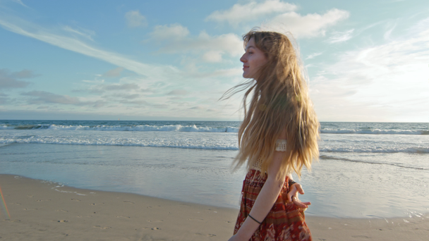 Szczęśliwa młoda kobieta z długimi włosami spacerująca po plaży - Materiał filmowy, wideo