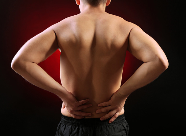 Young man with back pain, on red background - Foto, Imagen