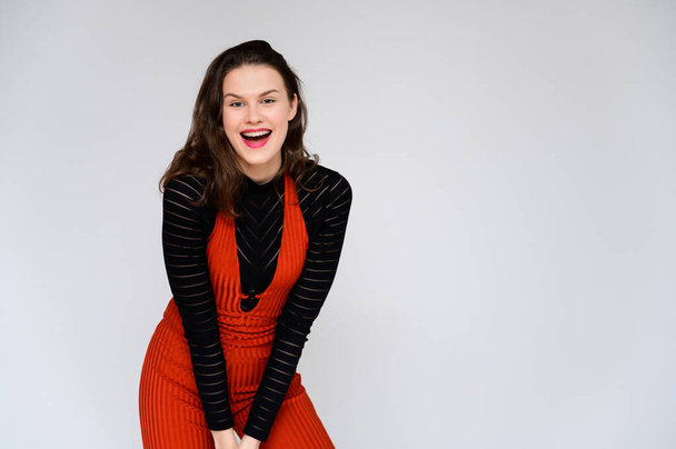 Concept adult girl on a white background. A photo of a pretty brunette girl in red trousers and a black sweater smiles and shows different emotions in different poses right in front of the camera. - Фото, зображення