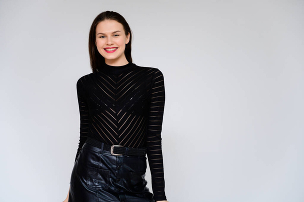 Concept adult girl on a white background. A photo of a pretty brunette girl in a black skirt and black sweater smiles and shows different emotions in different poses right in front of the camera. - Fotografie, Obrázek
