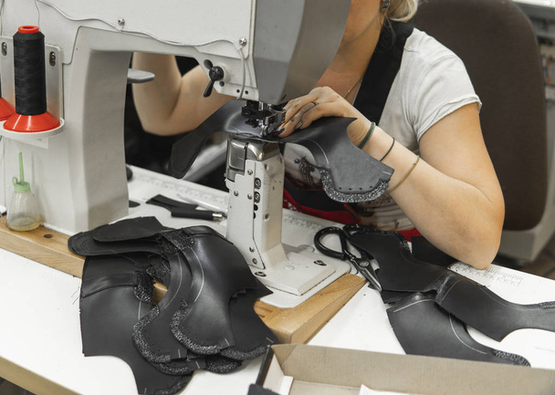 Macchina da cucire in un laboratorio in pelle in azione con le mani che lavorano su un dettaglio in pelle per scarpe. Mani delle donne con macchina da cucire alla fabbrica di scarpe
. - Foto, immagini