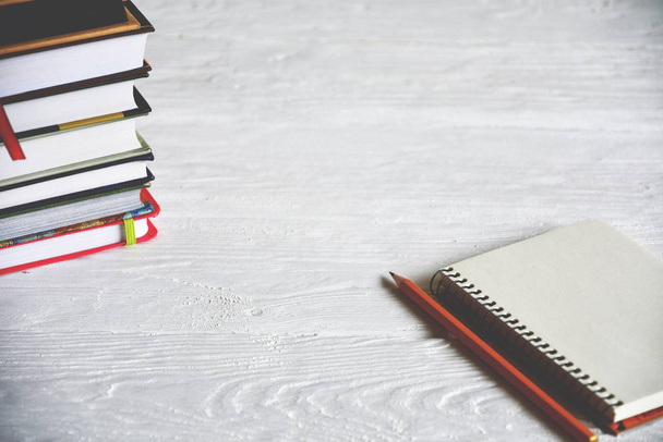Egy halom könyv, notebook és ceruza fehér fából készült háttérrel. - Fotó, kép