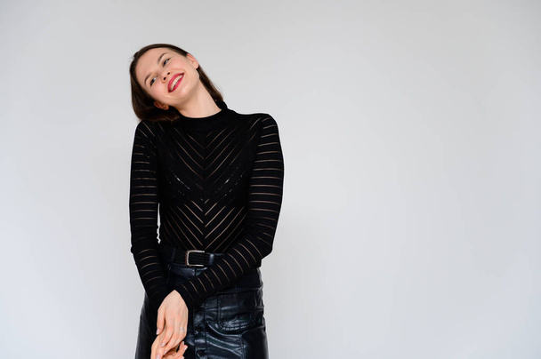 Concept adult girl on a white background. A photo of a pretty brunette girl in a black skirt and black sweater smiles and shows different emotions in different poses right in front of the camera. - Fotó, kép
