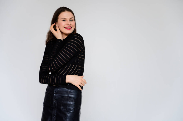 Concept adult girl on a white background. A photo of a pretty brunette girl in a black skirt and black sweater smiles and shows different emotions in different poses right in front of the camera. - Foto, Bild