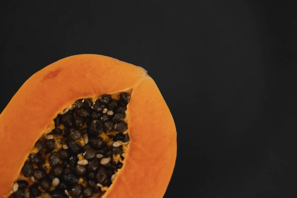 Half of ripe papaya with seed on a black plates and with a green plants on background. Slices of sweet papaya. Halved papayas. Healthy exotic fruits. Vegetarian food. - 写真・画像