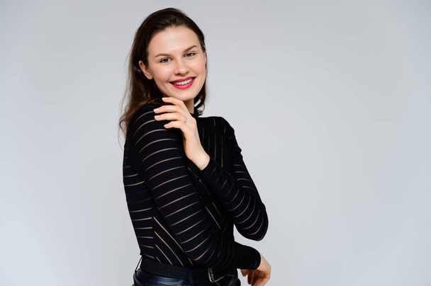 Concept adult girl on a white background. Large photo of a pretty brunette girl in a black sweater smiling and showing different emotions in different poses right in front of the camera. - Fotó, kép