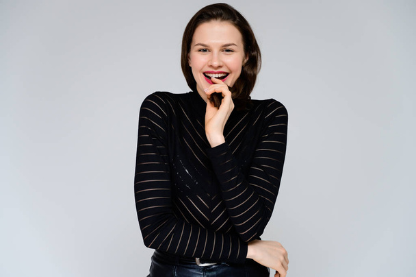 Concept adult girl on a white background. Large photo of a pretty brunette girl in a black sweater smiling and showing different emotions in different poses right in front of the camera. - Photo, image