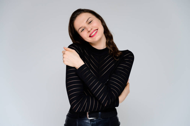 Concept adult girl on a white background. Large photo of a pretty brunette girl in a black sweater smiling and showing different emotions in different poses right in front of the camera. - Foto, afbeelding