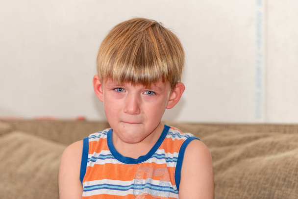Un niño triste y triste se sienta y llora en el sofá. - Foto, imagen