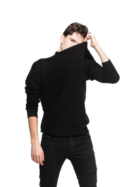 junges männliches Model in schwarzer Kleidung posiert vor weißem Studiohintergrund. Kaukasischer Typ in stylischer Kleidung, Pullover und Jeans. Mode-Modell junger weißer Mann - Foto, Bild