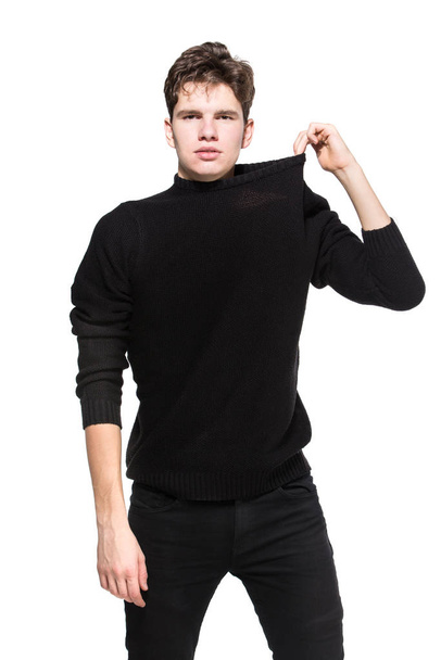Joven modelo masculino en ropa negra posando en un estudio de fondo blanco. Chico caucásico en ropa elegante suéter y jeans aislar. Modelo de moda joven hombre blanco
 - Foto, Imagen