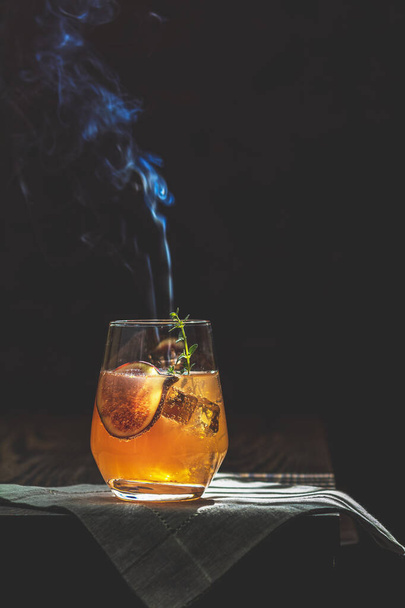 Pink cocktail with fig, thyme and ice in glass with smoke on dar - Photo, Image