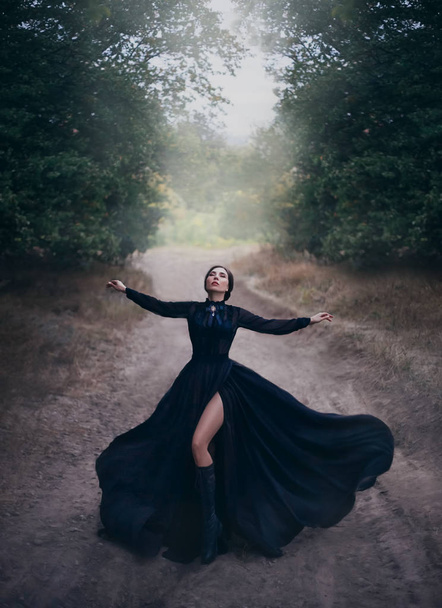 Gothic lady in black vintage silk flying dress, raises her hands in prayer.  - Photo, image