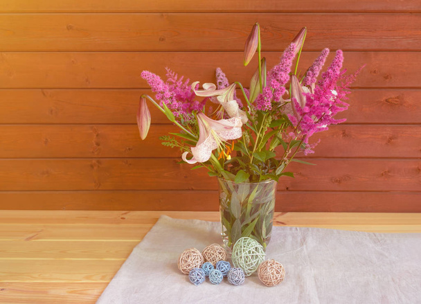 Bouquet of beige colored lilies with pink spots, pink spirea and astilbe flowers in glass vase and decorative balls near.  - Photo, Image