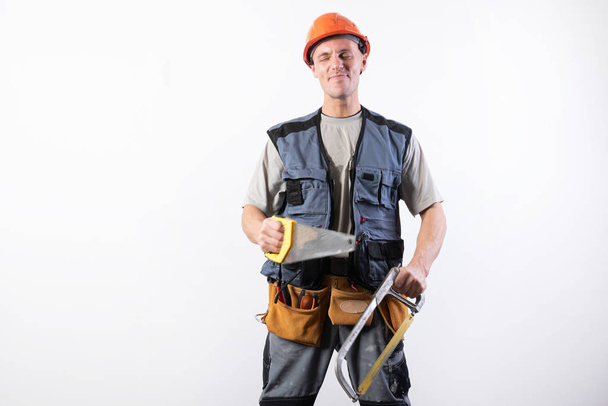 A builder with hacksaw in a helmet, smiling. On a light background. - Foto, Imagem