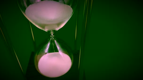 Hourglass on a stand, black background. Glass hourglass in the case. Glass time meter. Concept: time is running out, time management, time value - Footage, Video