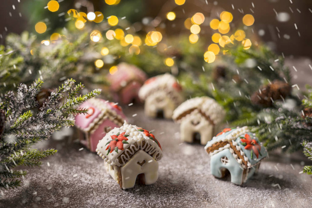 Miniatur-Lebkuchenhaus auf dem Hintergrund eines Weihnachtsbaums mit Lichtergirlanden. Schneefall-Effekt. - Foto, Bild
