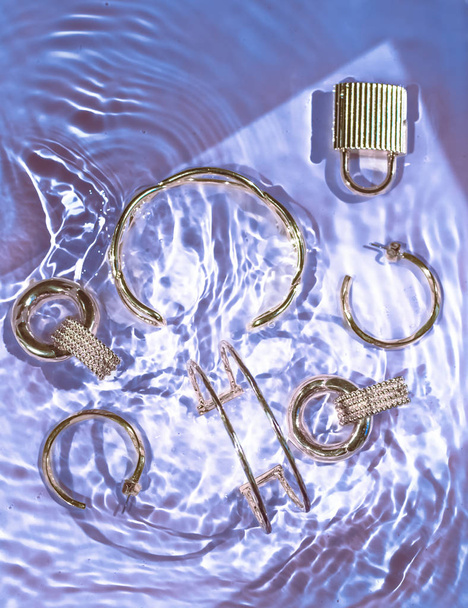 Pulseras de oro, pendientes, anillos, joyas en agua púrpura espalda
 - Foto, Imagen